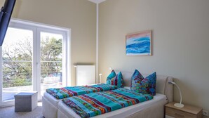 A bedroom with a large bed, a bedside table, a nightstand, a window with a view, and a painting on the wall. - Amselresidenz 5 - ADLERHORST (Binz)
