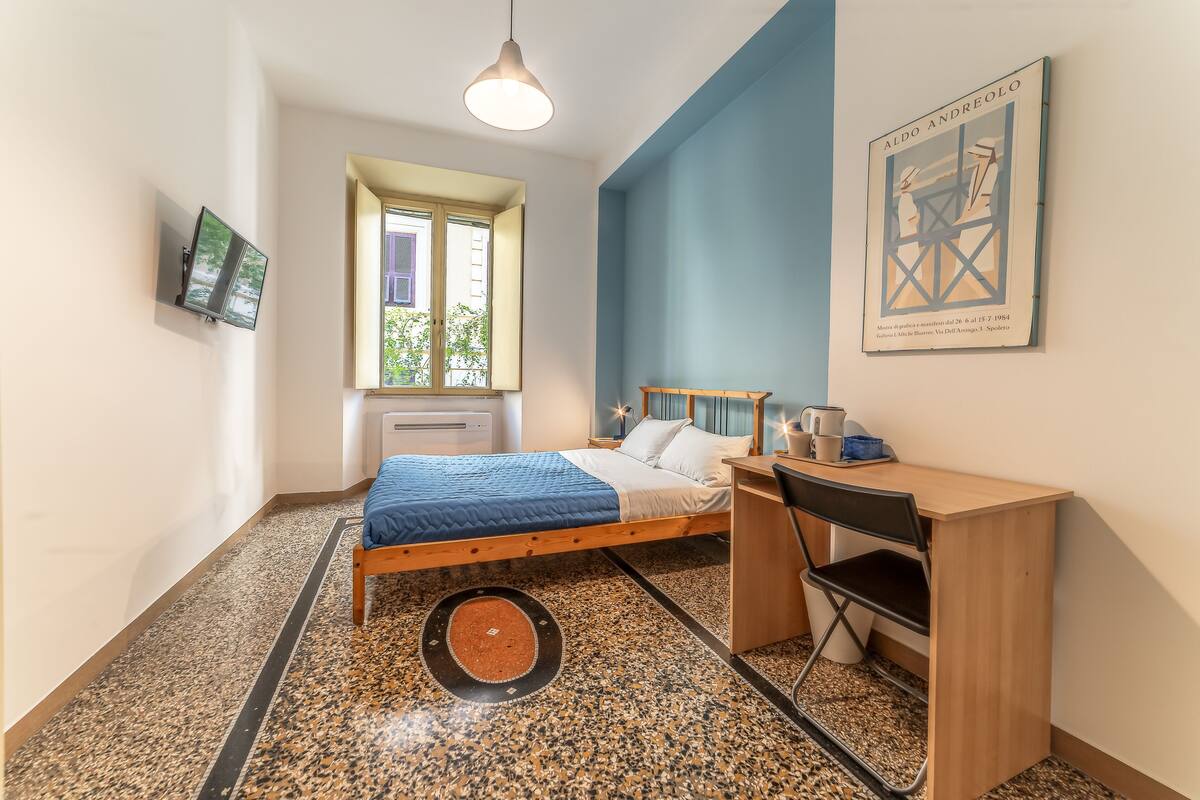 Een slaapkamer met een bed, een bureau, een stoel, een televisie en een raam.