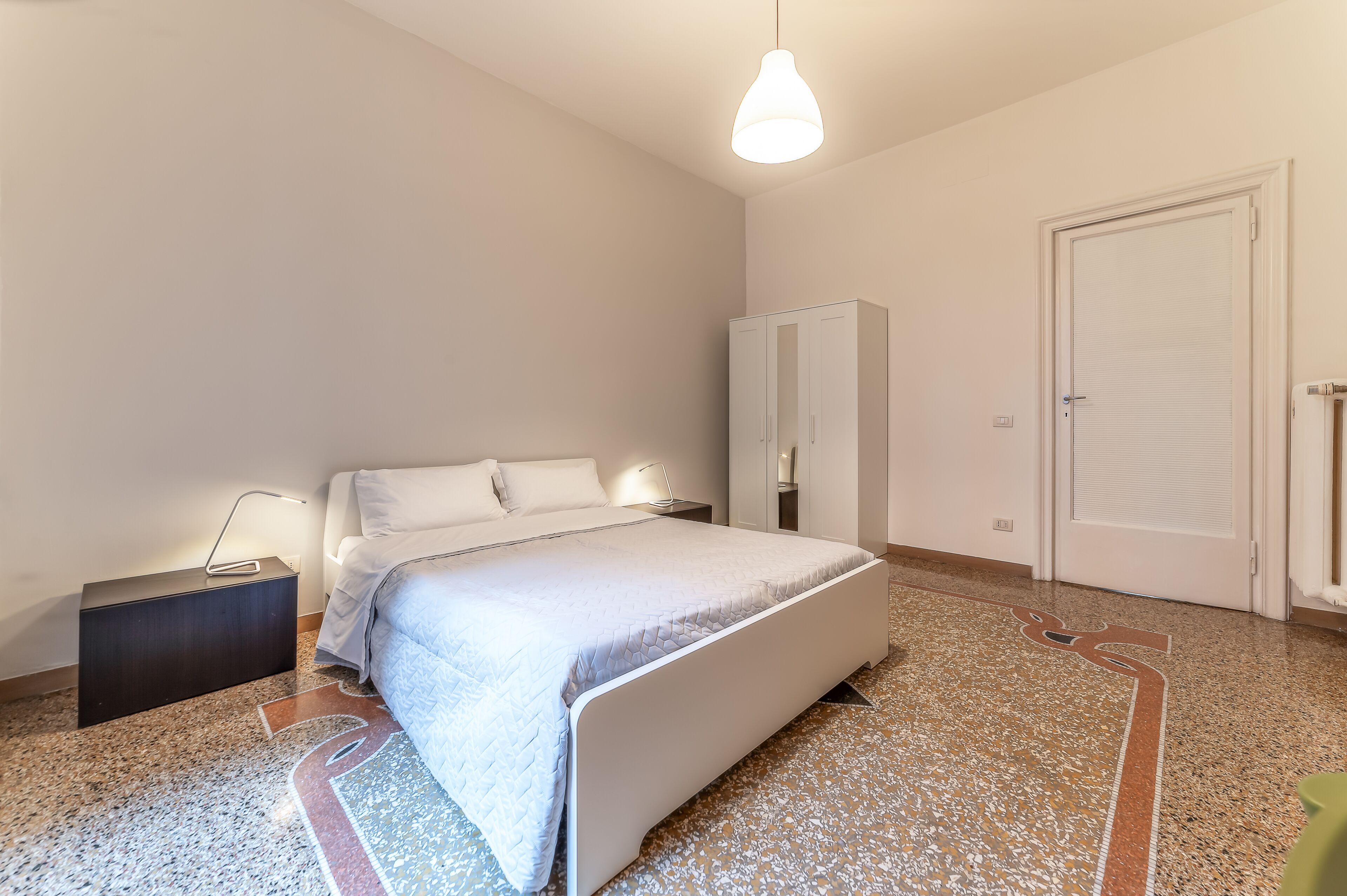 A bedroom with a bed, bedside table, wardrobe, and a door.