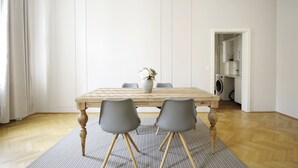 A dining area with a wooden table, four grey chairs, a vase with flowers, and a patterned rug. - HeyMi Apartments Karlsplatz (Vienna)