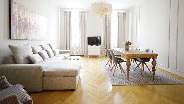 A modern living room with a sofa, a dining table with chairs, a TV, and a large abstract painting on the wall. - HeyMi Apartments Karlsplatz (Vienna)