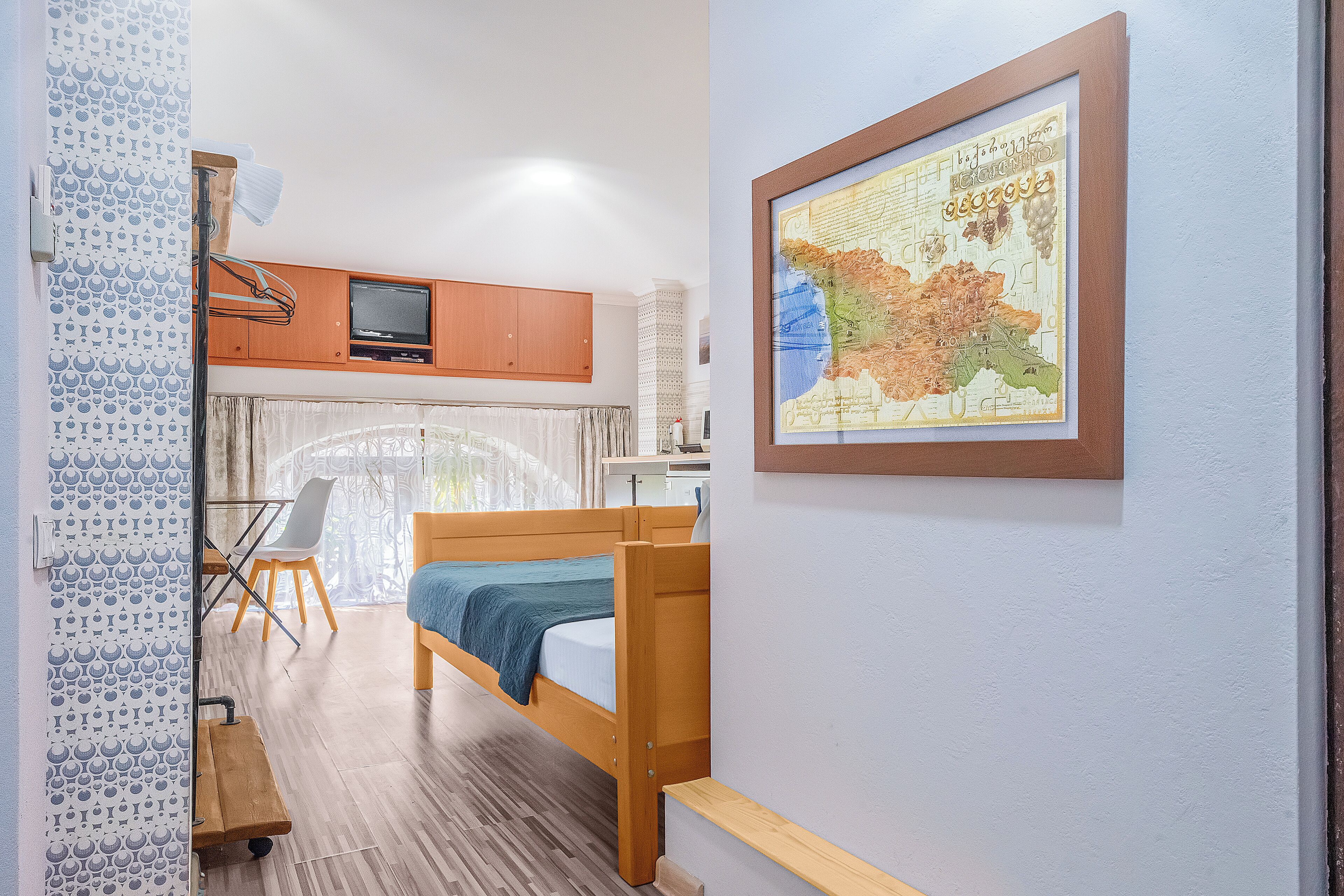 Een kleine kamer met een stapelbed, een bureau met stoel, een kaart aan de muur en een raam met gordijnen.