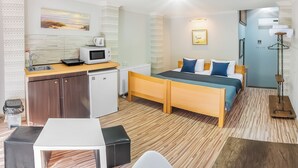 Une chambre d’hôtel compacte, dotée d’une kitchenette, d’un lit avec une literie bleue, d’une petite table et d’un lampadaire.