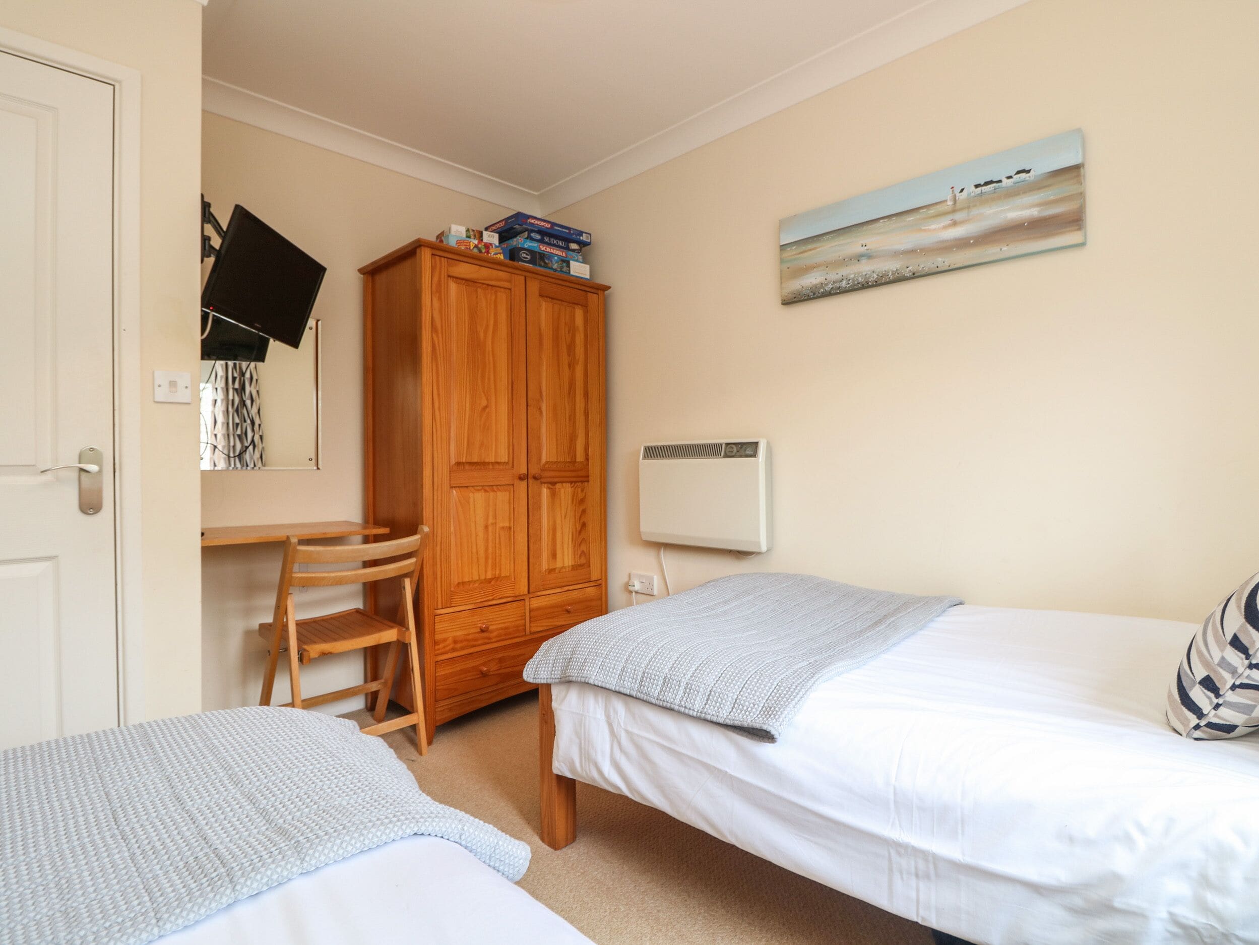 Een slaapkamer met twee bedden, een houten kledingkast, een bureau met stoel en een wandairconditioner.
