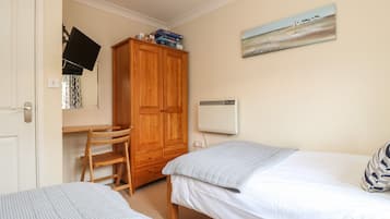 Een slaapkamer met twee bedden, een houten kledingkast, een bureau met stoel en een wandairconditioner.