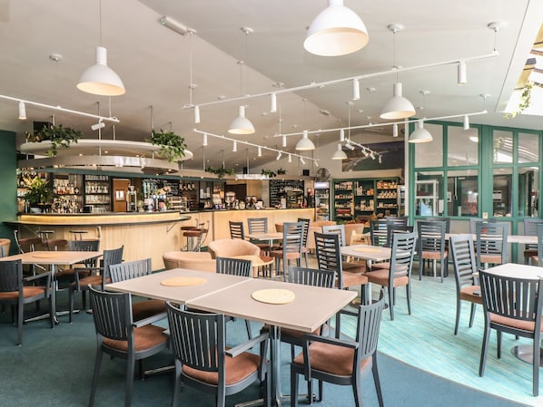 A modern cafe with multiple tables and chairs, a bar area, and large windows allowing natural light. - Manuka (Falmouth)