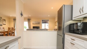 A compact kitchen with a refrigerator, microwave, and white cabinetry. - Manuka (Falmouth)