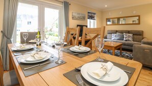 A dining area with a wooden table set for four, a grey sofa, and a grey armchair in the background. - Manuka (Falmouth)