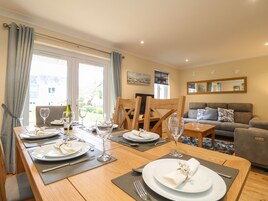 Un comedor con una mesa de madera preparada para cuatro personas, un sofá gris y un sillón gris al fondo.