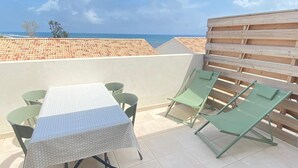 A terrace with a table and chairs, a wooden fence, and a view of the sea. - Tourné Vers le sud (Linguizzetta)