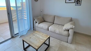 A living room with a beige sofa, a wooden coffee table, a woven pendant light, a sliding glass door, and two framed pictures on the wall. - Tourné Vers le sud (Linguizzetta)