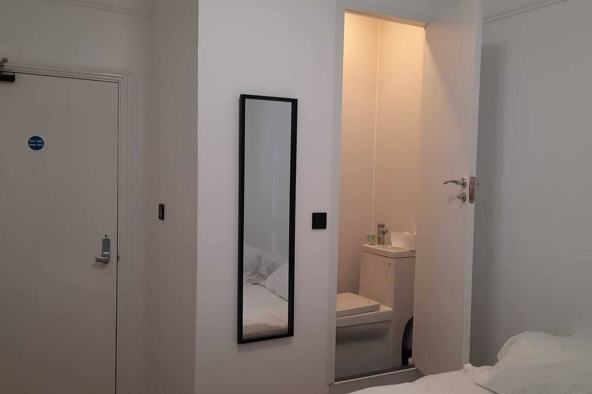 Een slaapkamer met een bed, een deur, een spiegel en een zichtbare badkamer door een open deur.