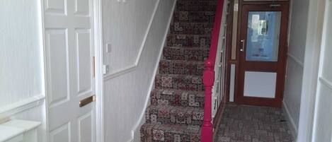A hallway with a patterned carpet, a white door, and a staircase with a red handrail.