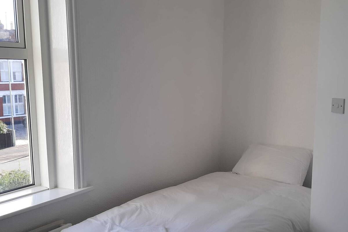 Een kleine kamer met een enkel bed, witte beddengoed en een raam.