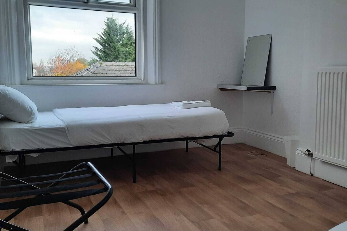 Een slaapkamer met een enkel bed, een raam met uitzicht op bomen, een radiator en een spiegel aan de muur.