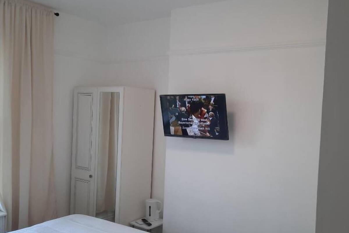 Hotelkamer met een bed, een aan de muur bevestigde televisie, een deur en een klein tafeltje met een afstandsbediening.