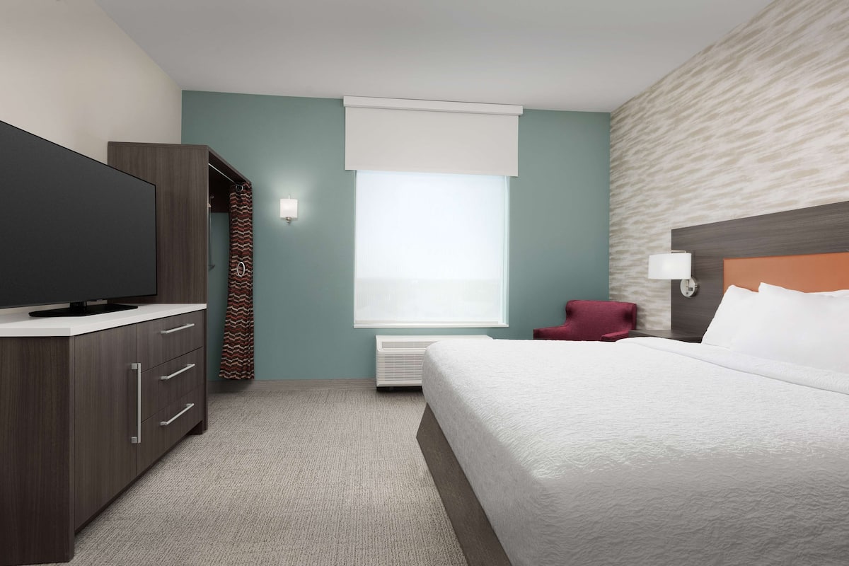 Een hotelkamer met een bed, televisie, garderobe, stoel en raam met jaloezieën.