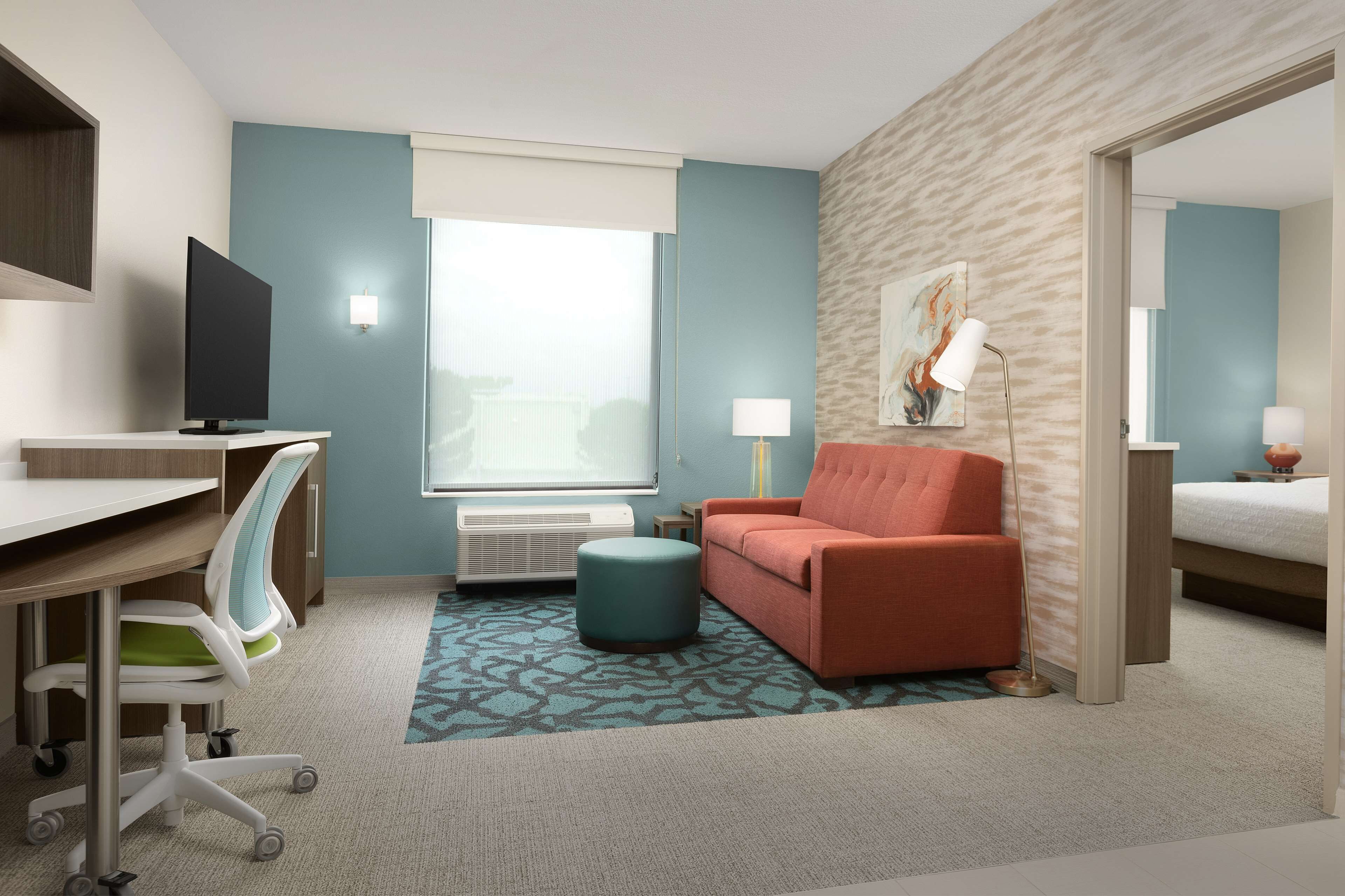 Een hotelkamer met een bureau, een televisie, een bank, een lamp en een bed.
