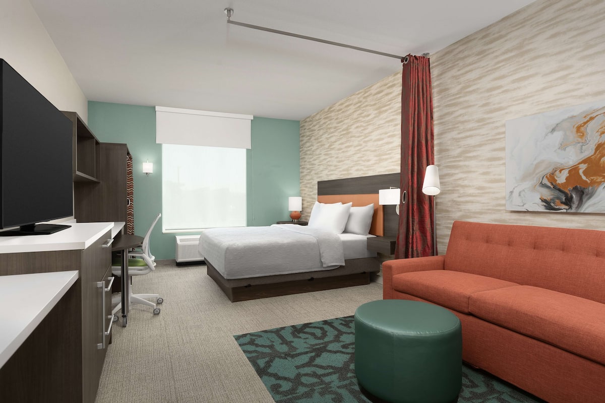 Een hotelkamer met een bed, een bureau, een televisie, een bank en een schilderij aan de muur.