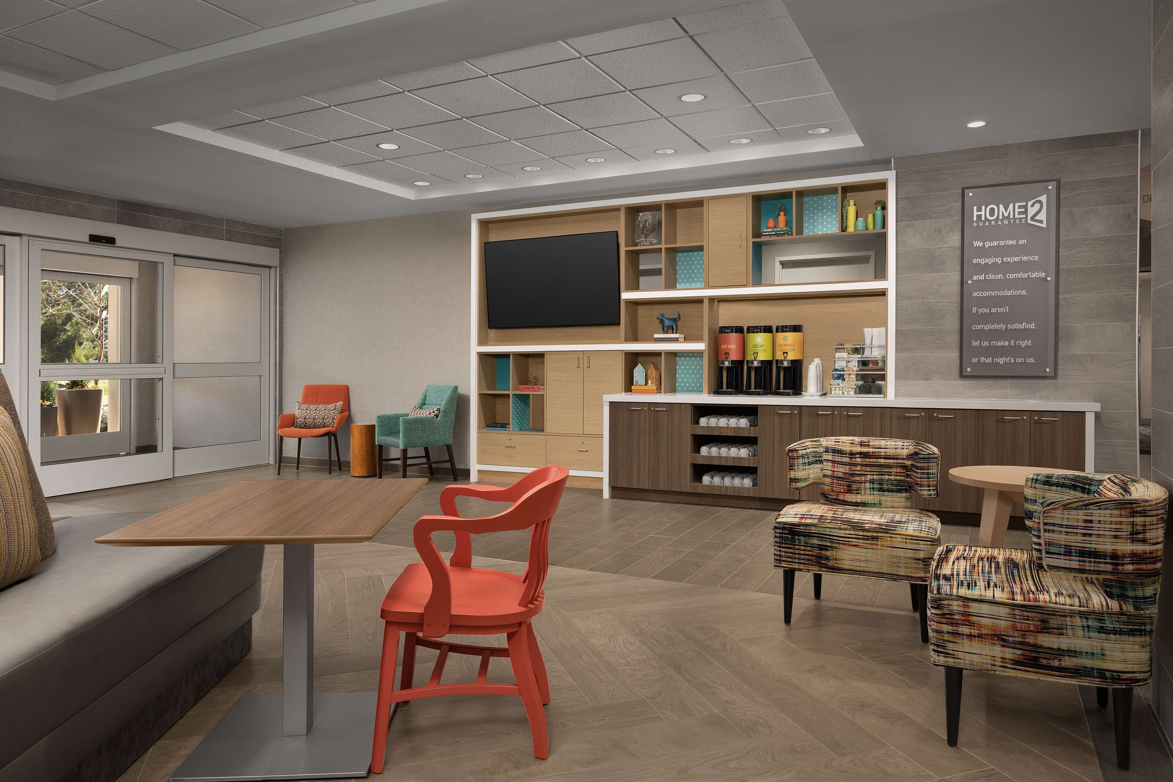A modern hotel room with a sofa, a dining table with chairs, a kitchen area with cabinets and a TV, and a sign on the wall.