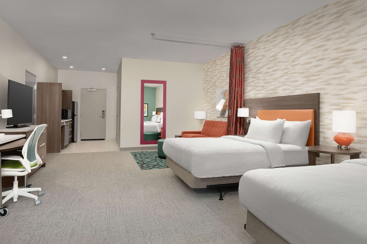Hotelkamer met twee bedden, een bureau, een stoel, een televisietoestel en een badkamer zichtbaar achter een deur.