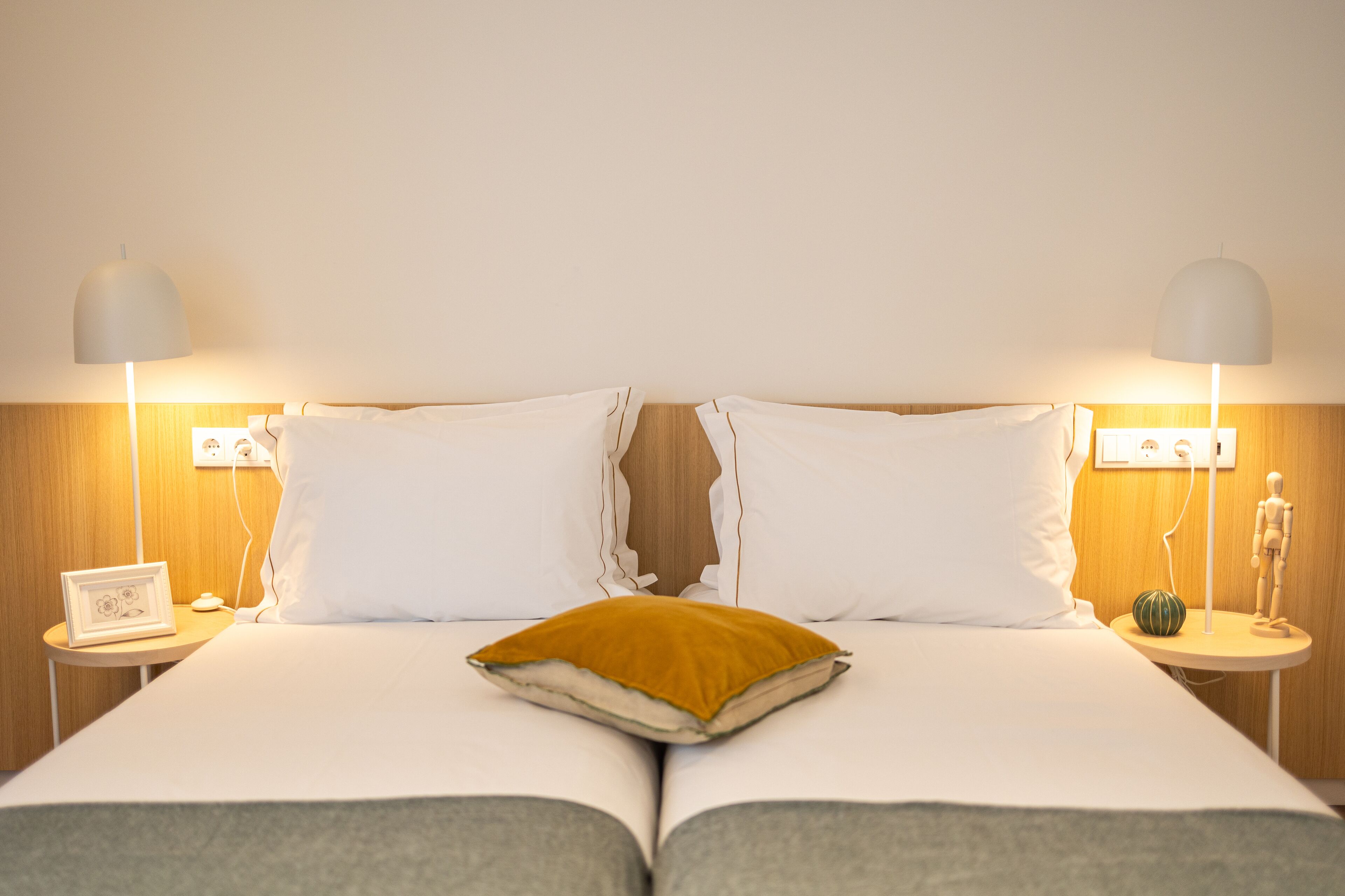 A double bed with white linens, two bedside tables with lamps, and a single mustard-colored pillow.