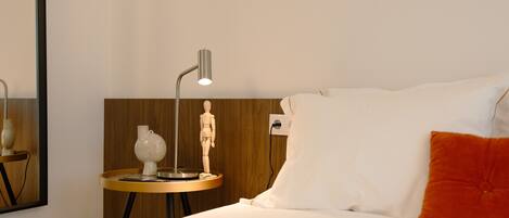 A hotel room with a bed, a wooden headboard, a bedside table with a lamp, a small sculpture, and a mirror.