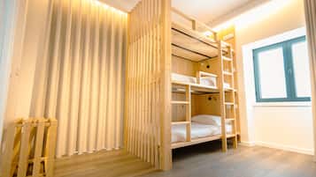 Habitación con literas, una escalera de madera, cortinas en la ventana y suelo de madera.