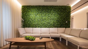 A modern living room with a green leafy wall, a beige sofa, and a wooden coffee table. - Watts House (Seia)