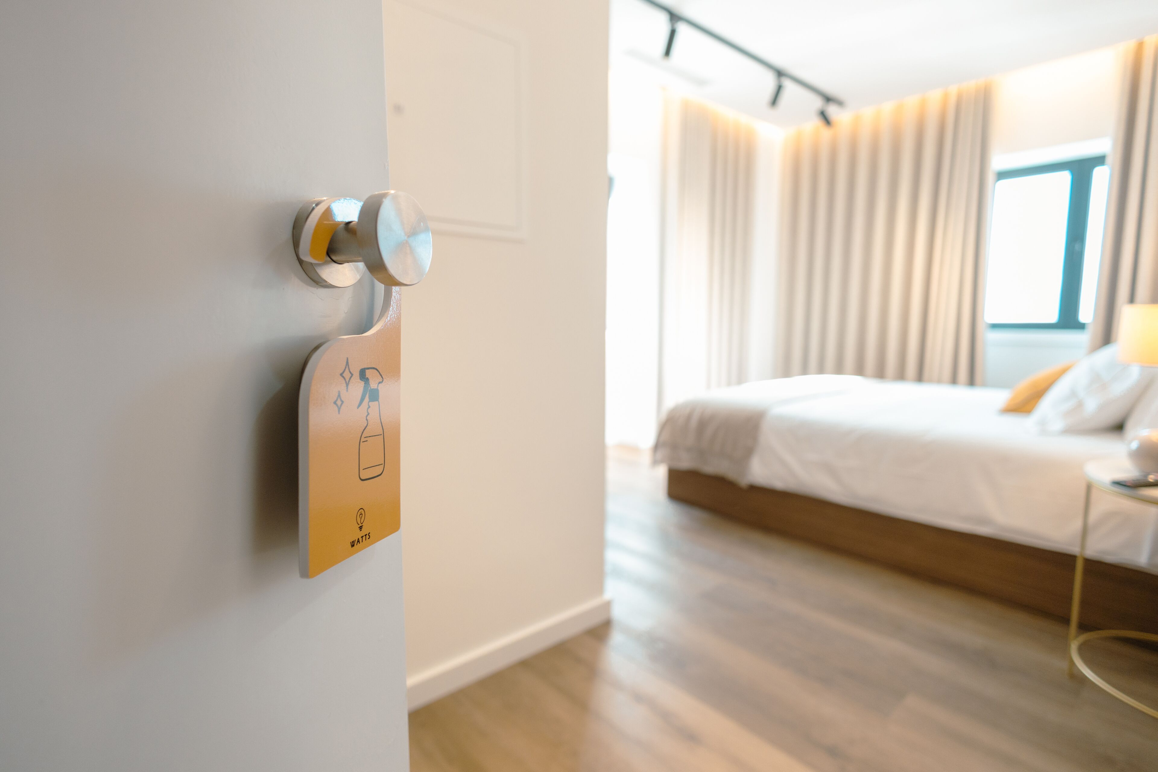 A modern hotel room with a wooden floor, a bed with white bedding, and a view of the outdoors through a window.