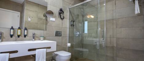 A modern bathroom with a glass-enclosed shower, a white sink with multiple bottles, and a toilet.