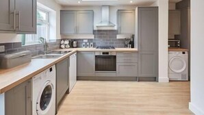 A modern kitchen with grey cabinets, a built-in oven, and a dishwasher. - Elfleda Stay | Modern 5 bedroom house (Cambridge)