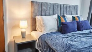 A hotel room with a bed, a nightstand with a lamp, and a headboard. - Elfleda Stay | Modern 5 bedroom house (Cambridge)