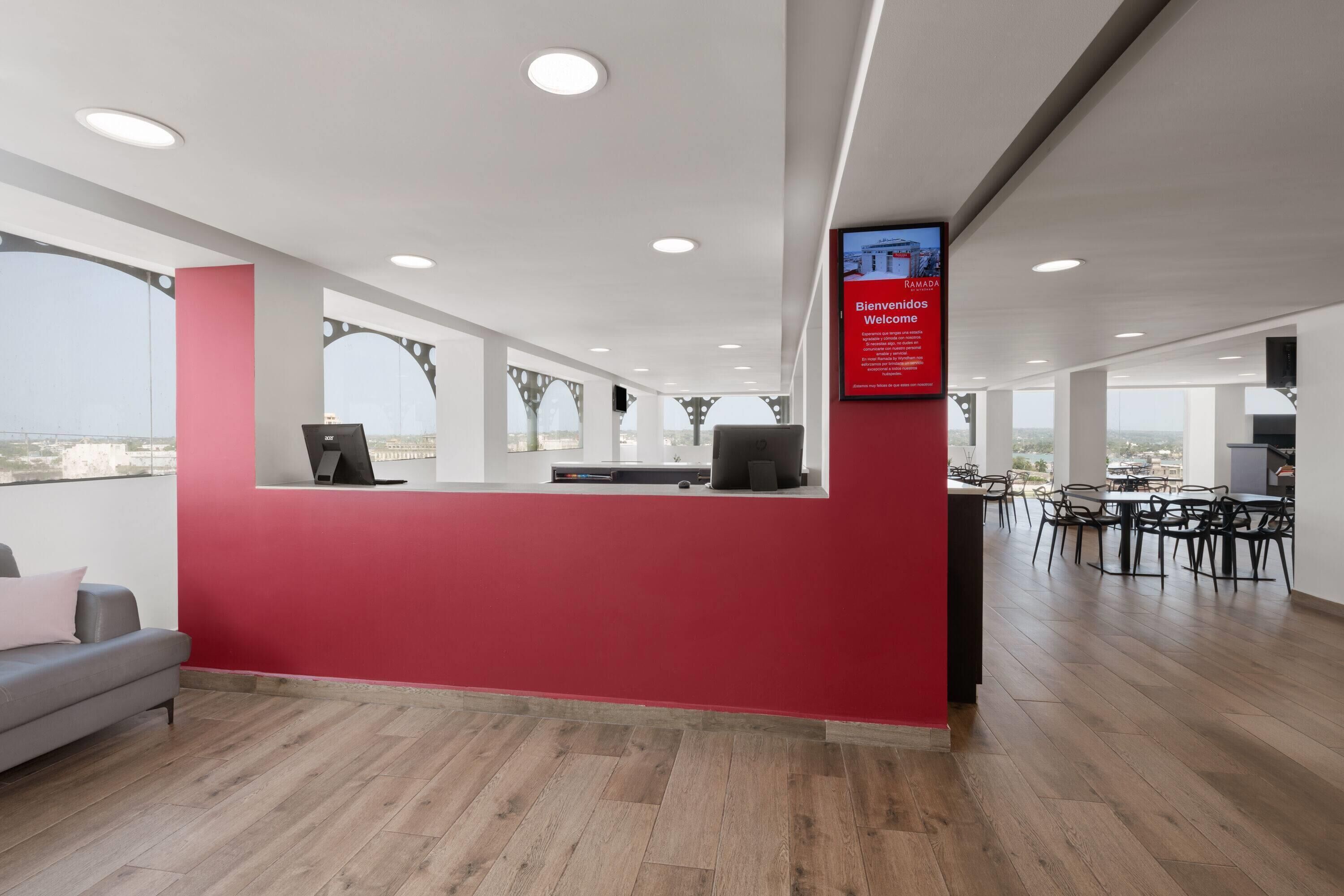 A modern reception area with a red wall, a computer desk, and a seating area.