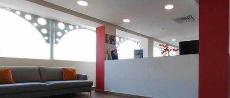 A modern reception area with a grey sofa, wooden flooring, and a red accent wall.