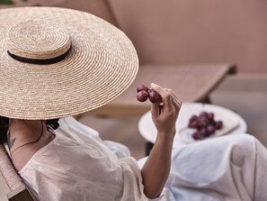 A person holding a bunch of grapes, seated in a chair with a white tablecloth, and a plate of grapes in the background.