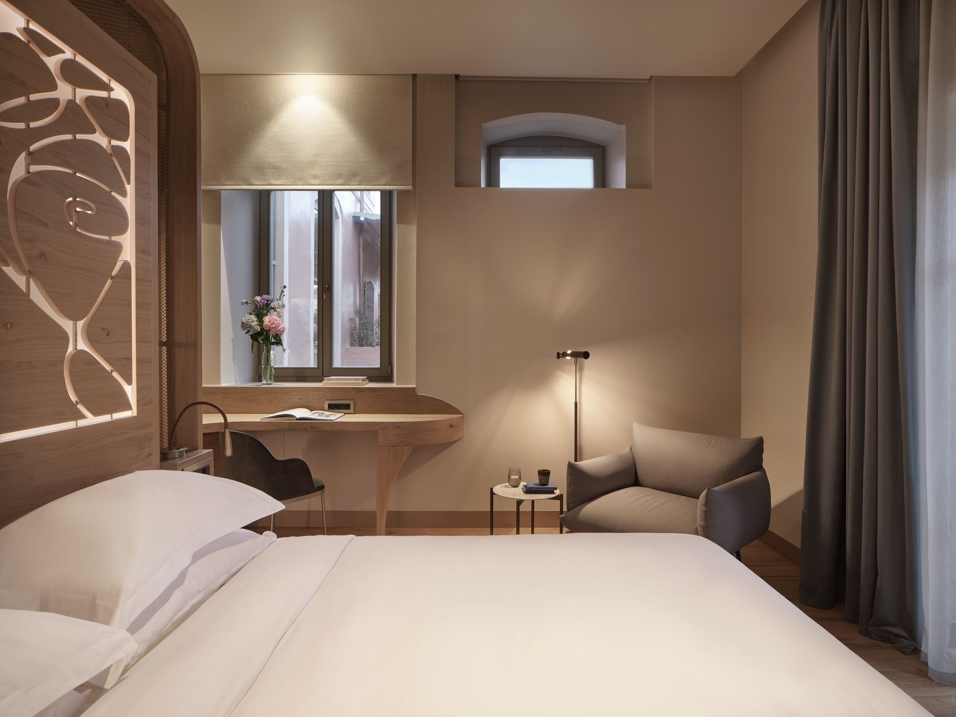 Habitación de hotel con cama, escritorio, silla y una mesita de noche con lámpara.