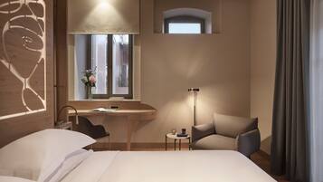 Habitación de hotel con cama, escritorio, silla y una mesita de noche con lámpara.