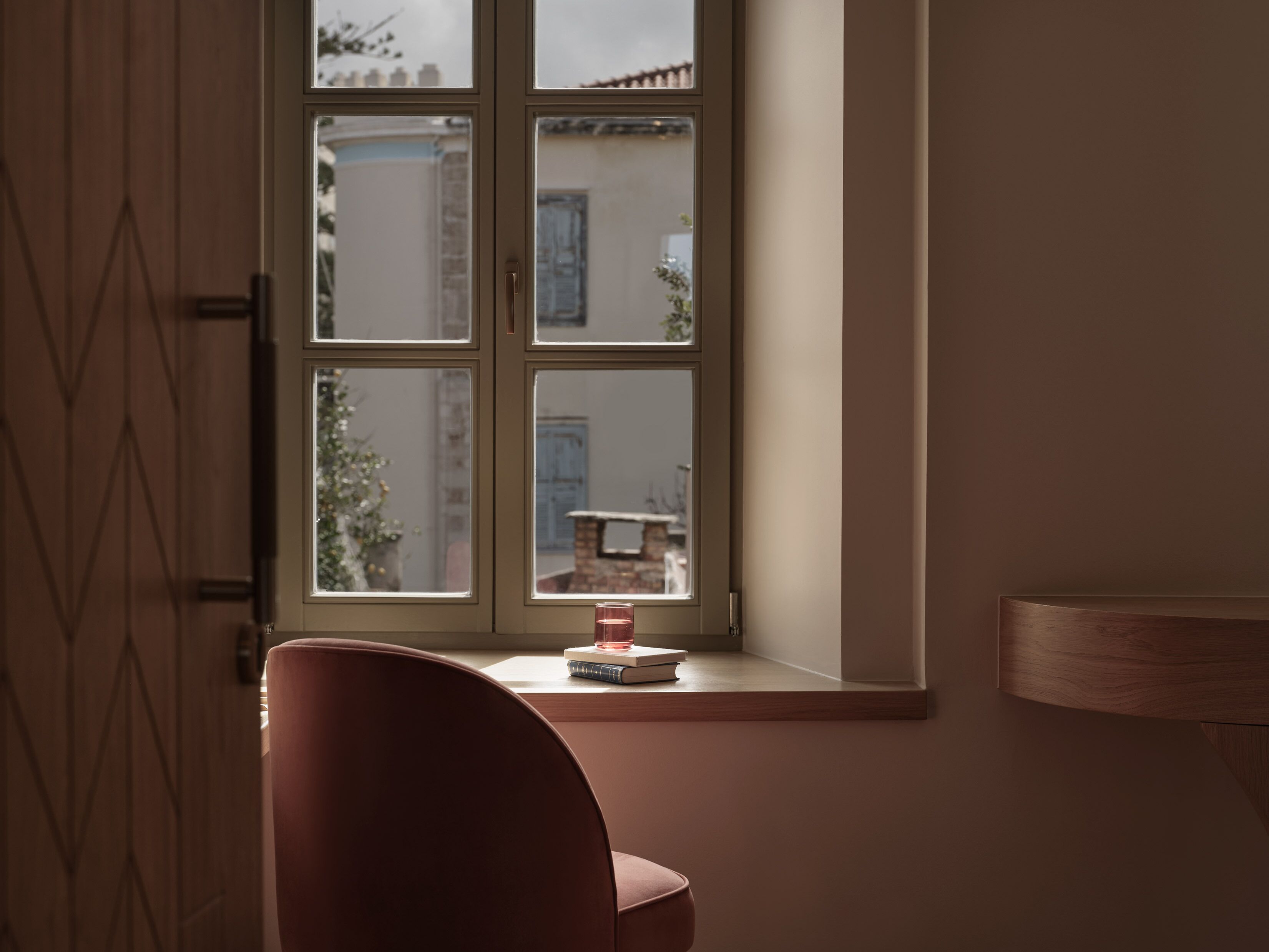 A room with a window, a chair, and a small table with books and a candle.