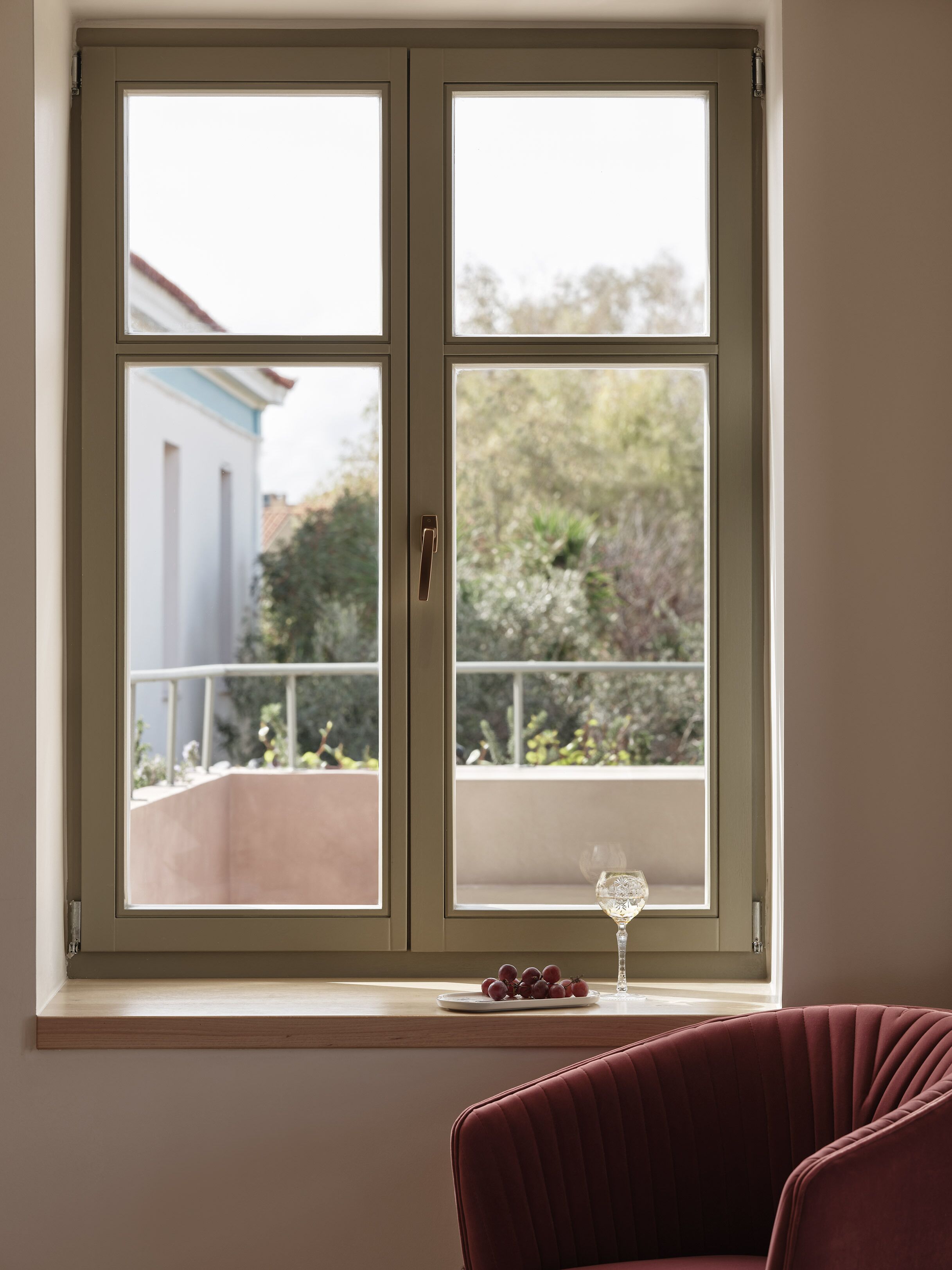A room with a window overlooking a balcony, a glass of water, and a plate of grapes on the windowsill.