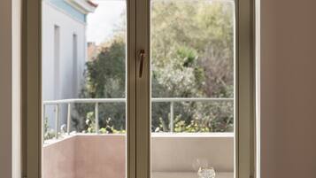 A room with a window overlooking a balcony, a glass of water, and a plate of grapes on the windowsill.