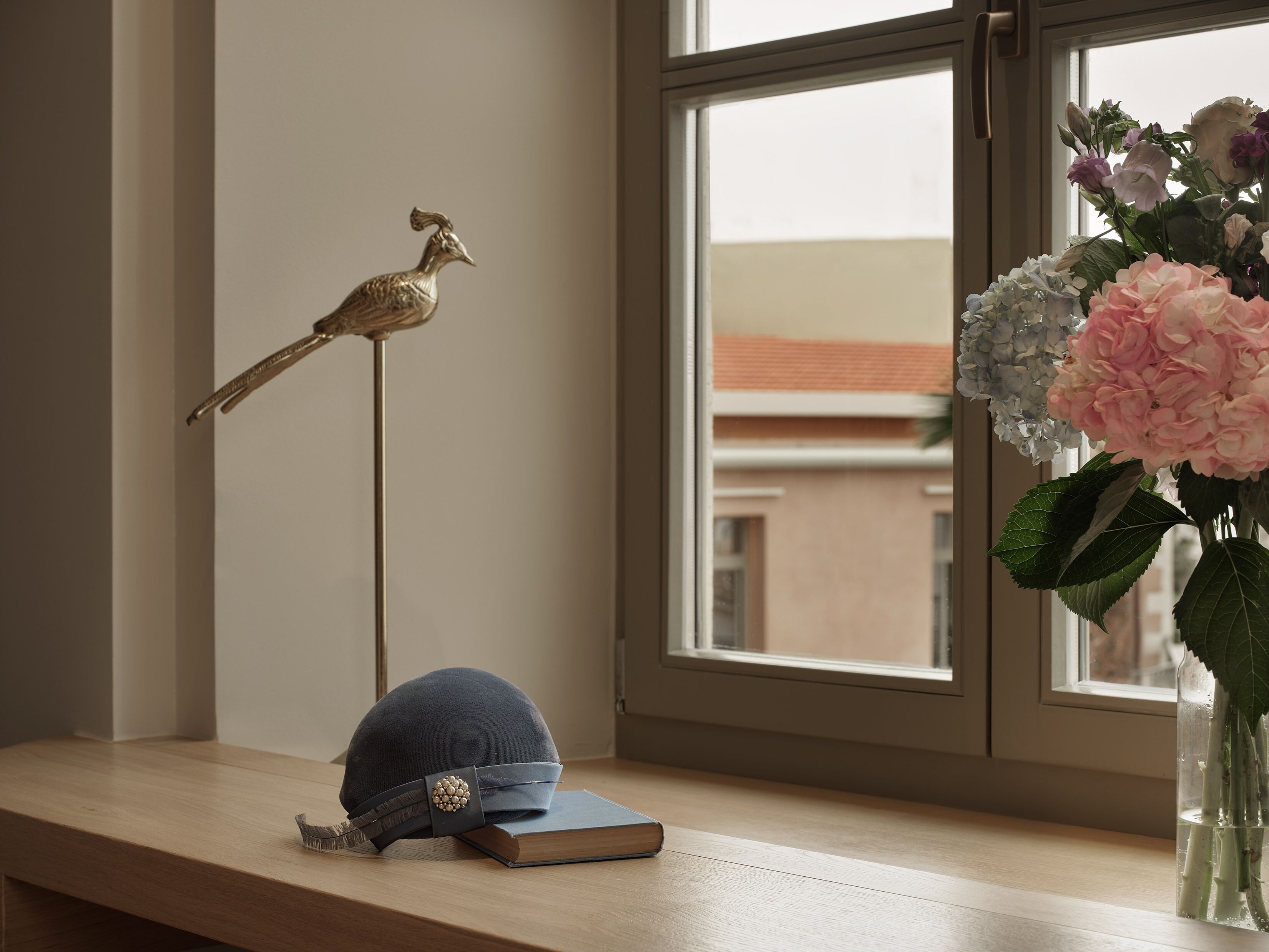Un escritorio con un libro, un sombrero azul y una figurita de pájaro decorativa.