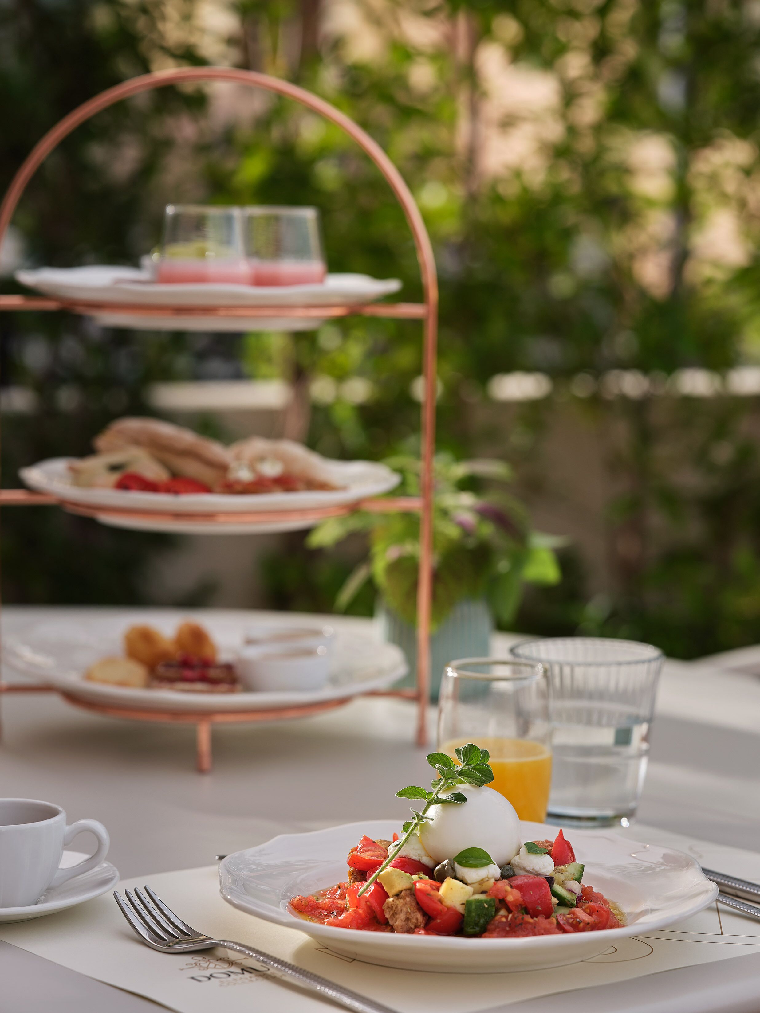 A three-tiered outdoor dining setup with plates of food and a glass of juice.