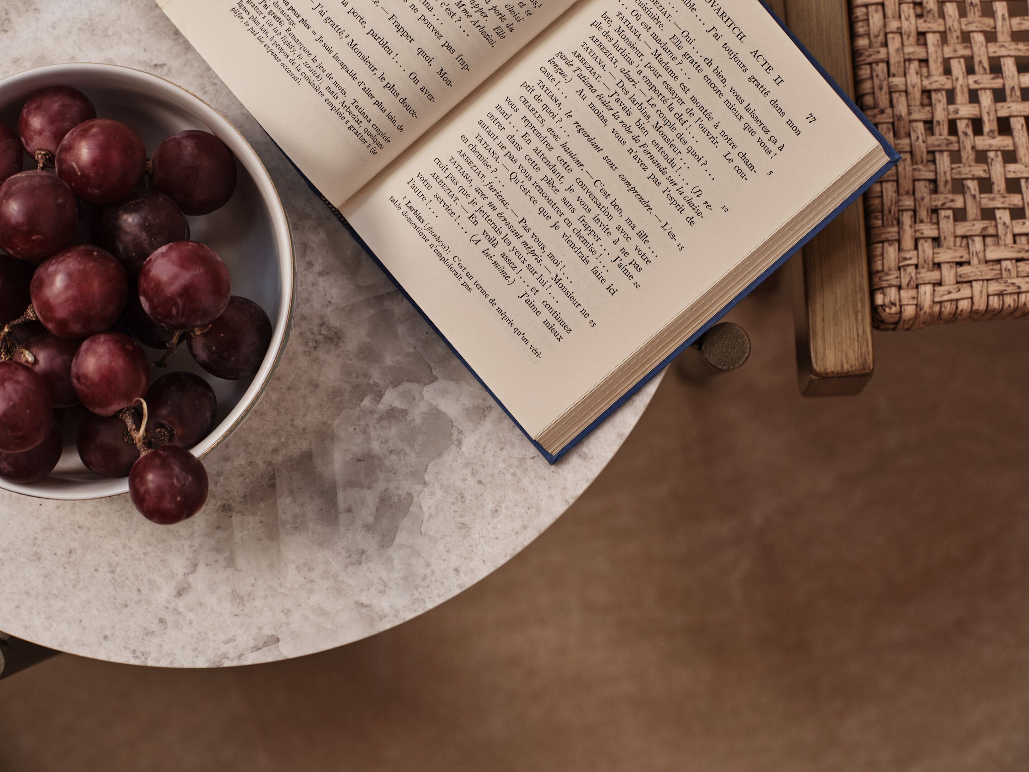 An open book with text on a round table next to a bowl of grapes.