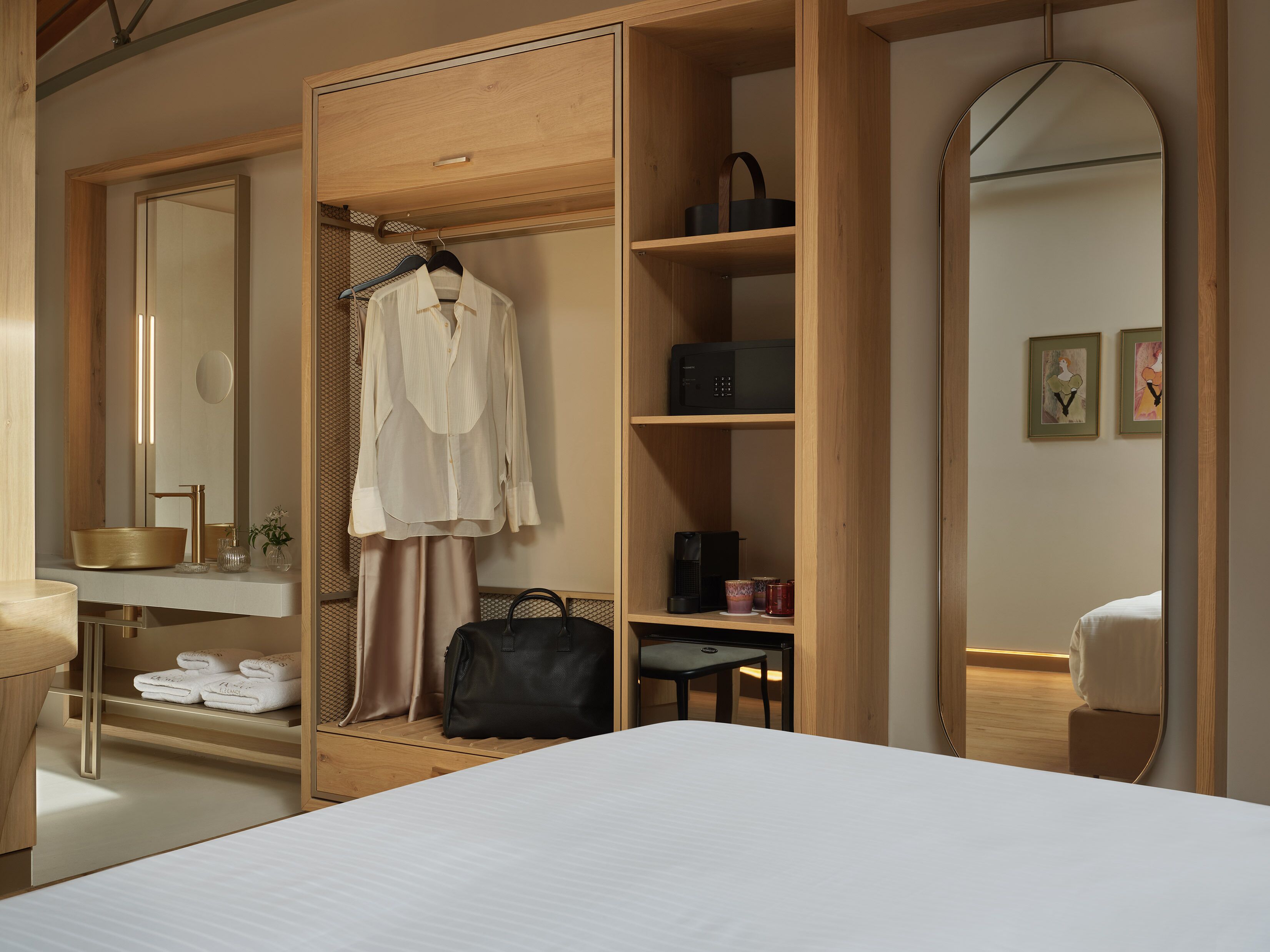 Une chambre moderne avec un grand lit, une armoire en bois, une coiffeuse avec un miroir et une petite table sur laquelle se trouvent une bouilloire et des tasses.