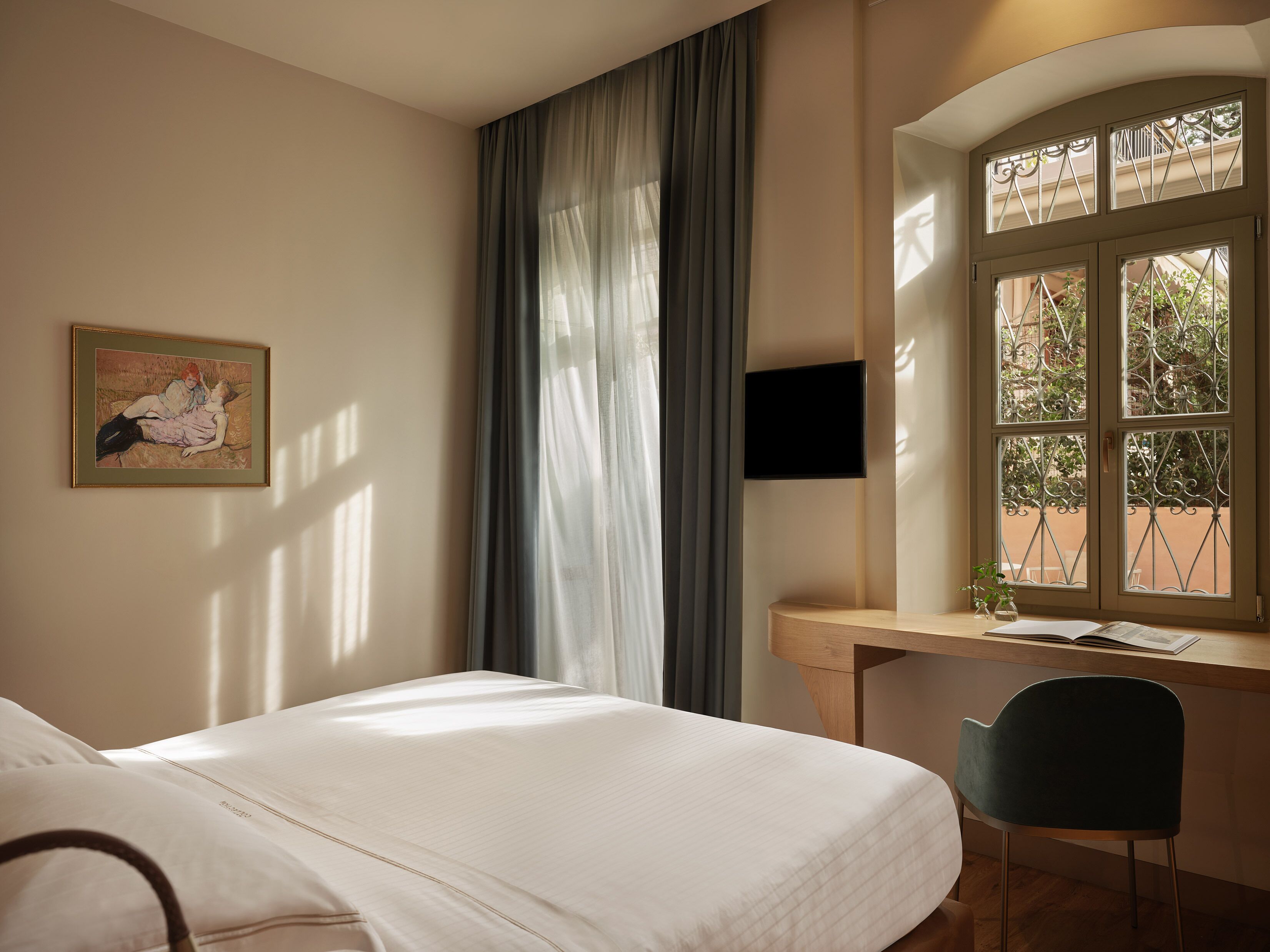 Habitación de hotel con cama, escritorio y silla, televisor y ventana con vista al exterior.