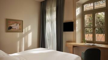 Habitación de hotel con cama, escritorio y silla, televisor y ventana con vista al exterior.