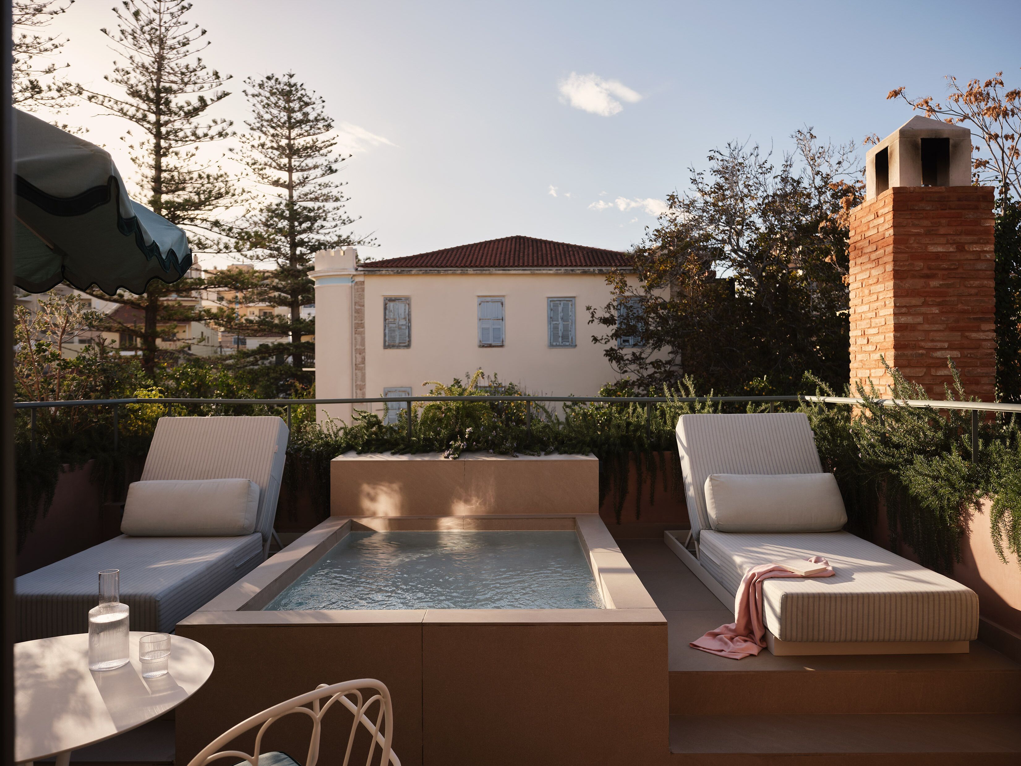 Eine Dachterrasse mit rechteckigem Pool, zwei Sitzbereichen mit Kissen und einem Backsteinsschornstein.