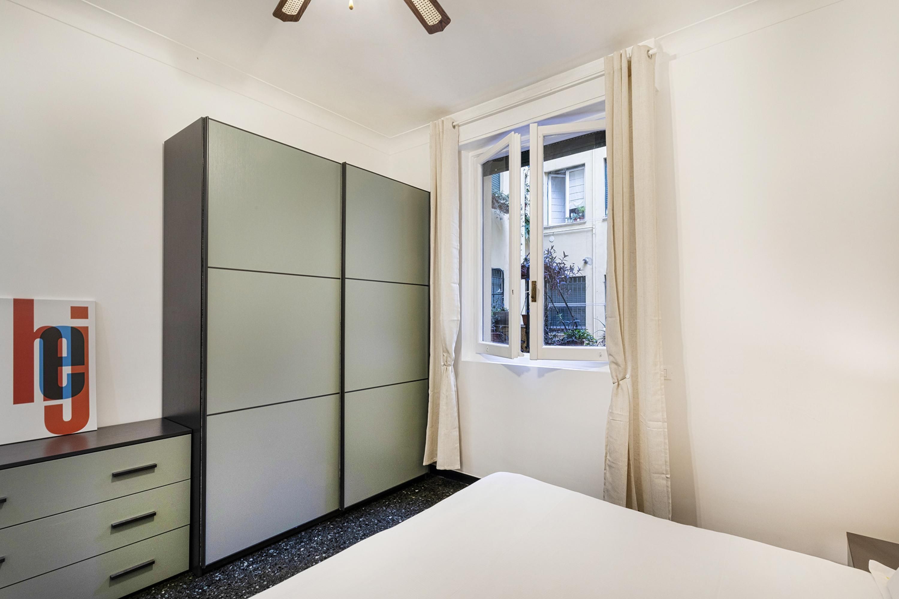 A bedroom with a bed, a wardrobe, a dresser, and a window with curtains.