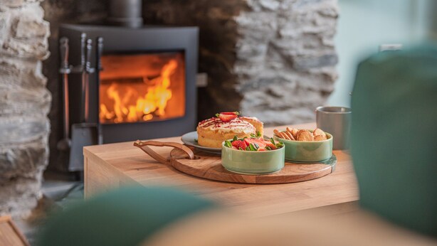 Ein gemütlicher Raum mit einem Kamin aus Stein, einem Holztisch mit Kuchen und zwei Schüsseln voller Essen.